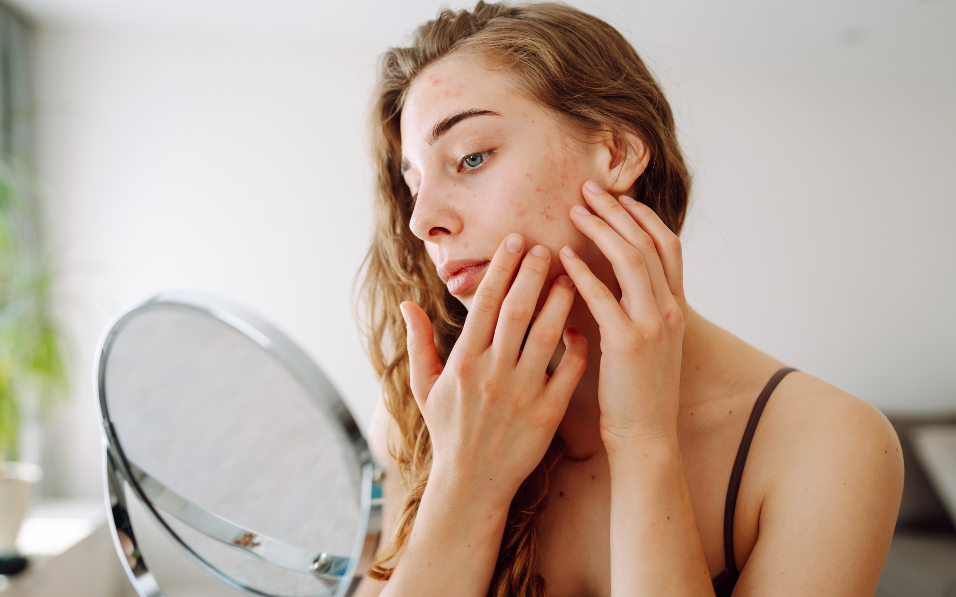 Woman gently touching dry skin in front of a bathroom mirror.