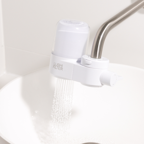 White faucet filter being used on a kitchen sink with water flowing.