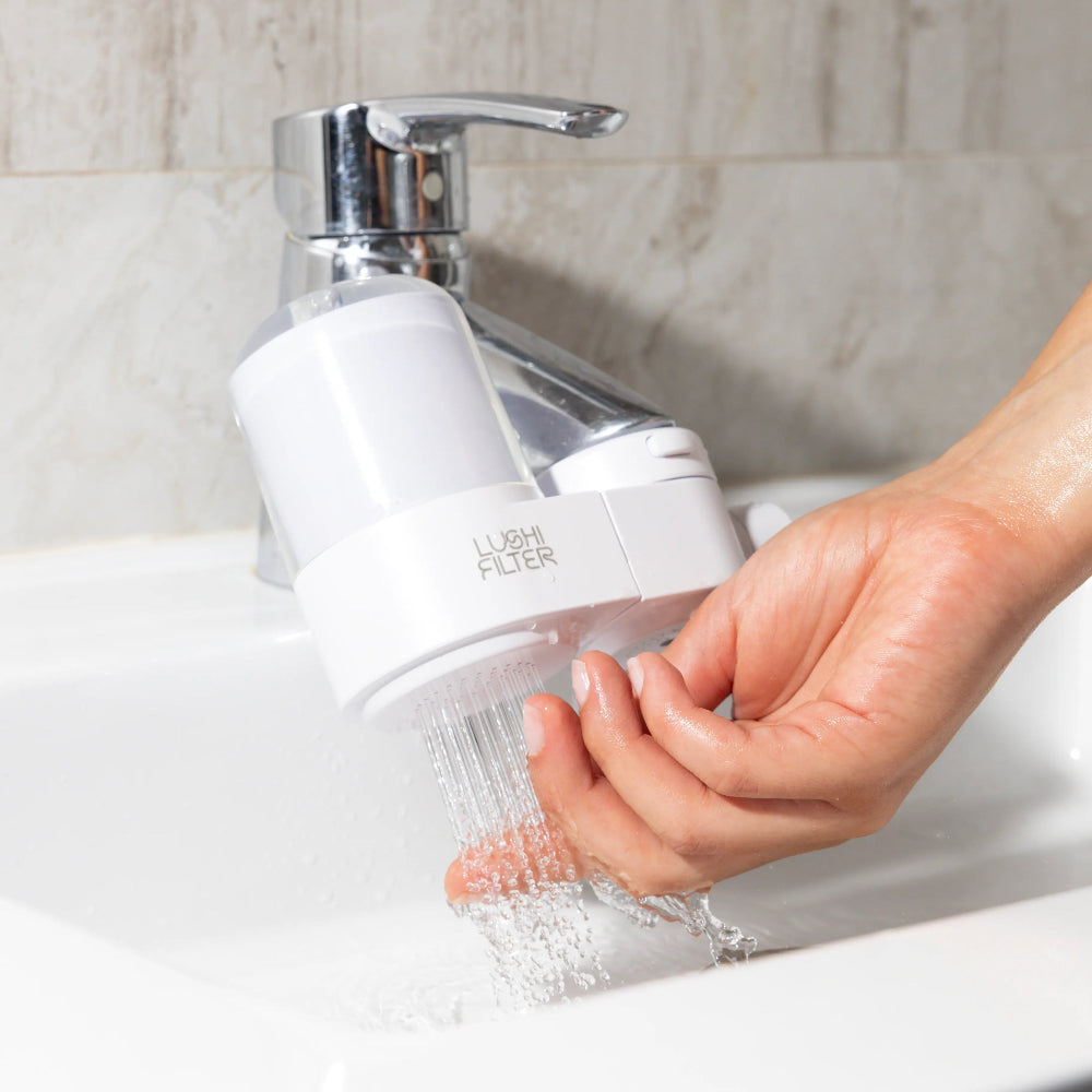 Hand washing a clear water filter with a white base, mounted on a sink tap.